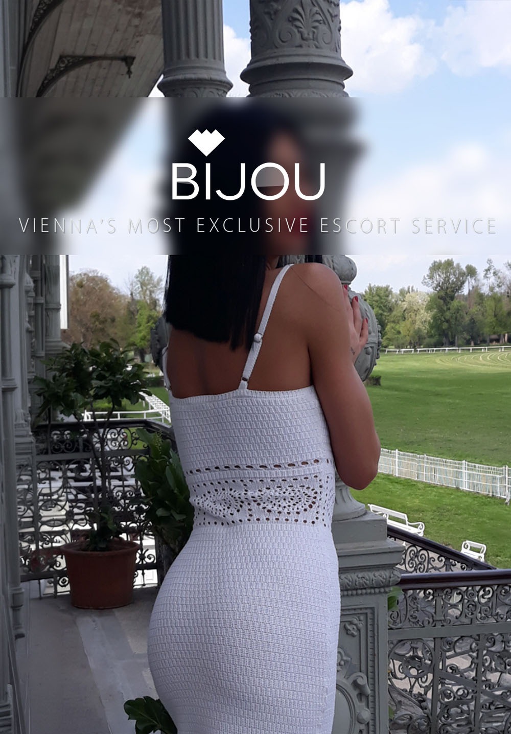 Eine Frau in einem weißen Kleid steht auf einer Terrasse mit Blick auf einen grünen Park. Im Hintergrund sind Säulen und ein blauer Himmel zu sehen.