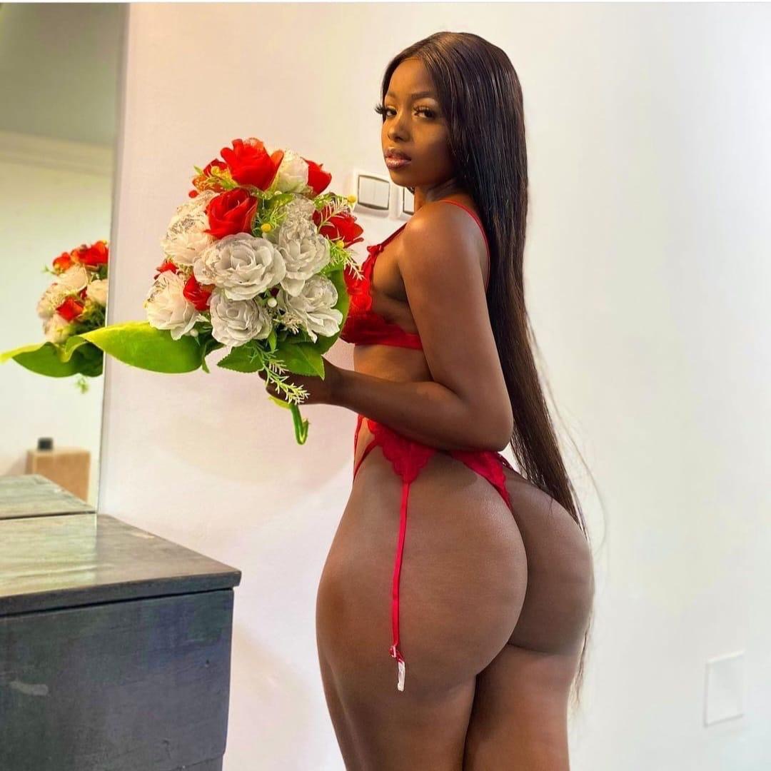 Eine Frau mit rotem Slip hält einen Blumenstrauß aus roten und weißen Rosen. Sie steht in einem hellen Raum, frontal zur Kamera.