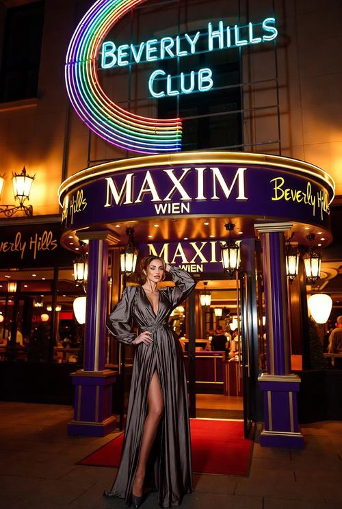 Eine Frau in einem eleganten Kleid steht vor dem Eingang des "Maxim Wien" mit leuchtendem Neon-Schild "Beverly Hills Club".