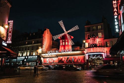Nachtansicht des Moulin Rouge in Paris mit beleuchtetem Windmühlen-Dach und roter Fassade.
