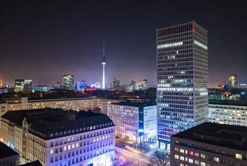 Nachtstadtansicht mit beleuchteten Hochhäusern, im Hintergrund der Fernsehturm Berlin.