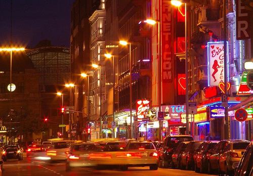 Bunte Abendstraße mit Neonlichtern, Autos und beleuchteten Geschäftsschildern.